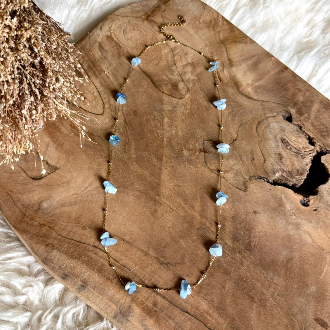 Lange goudkleurige Lumi-ketting met aquamarijn op een houten schaal