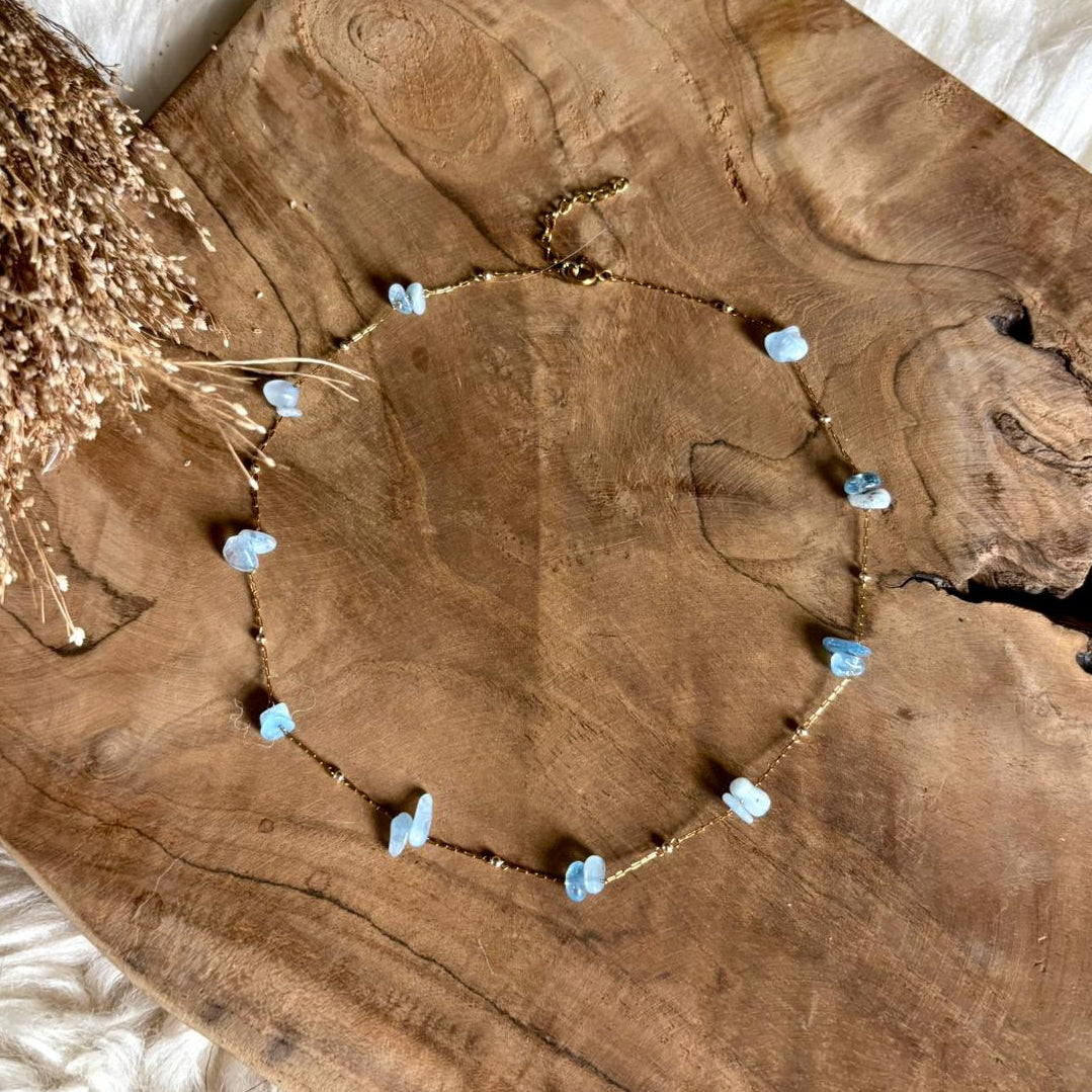 Korte goudkleurige Lumi-ketting met aquamarijn op een houten schaal