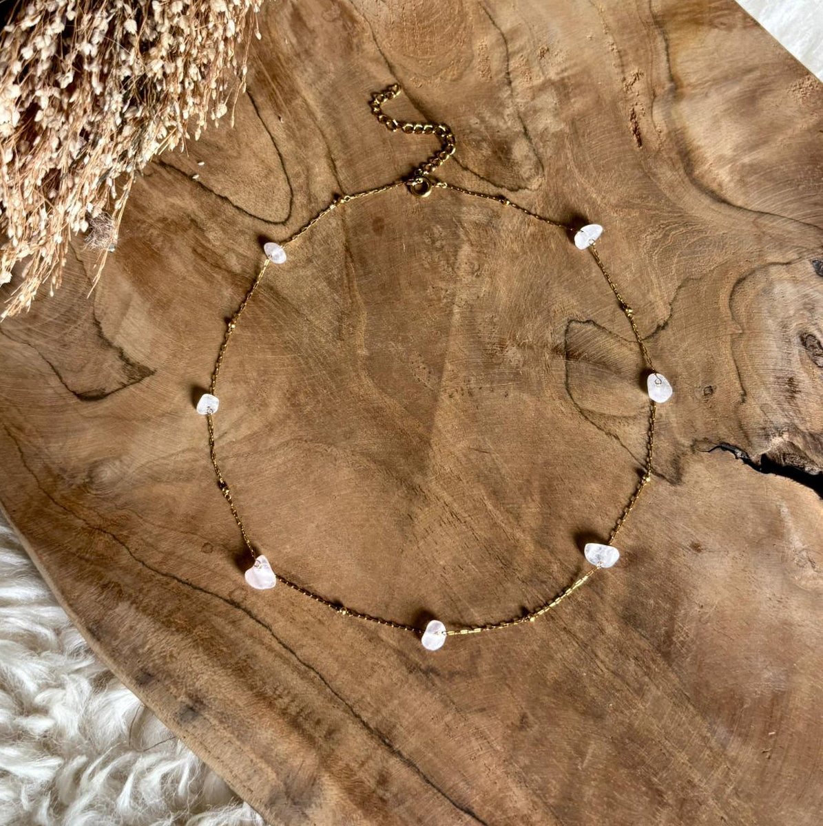 Goudkleurige ketting Alba met ronde rozenkwarts op een houten schaal