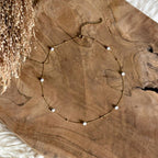 Goudkleurige ketting Alba met witte howliet op een houten schaal