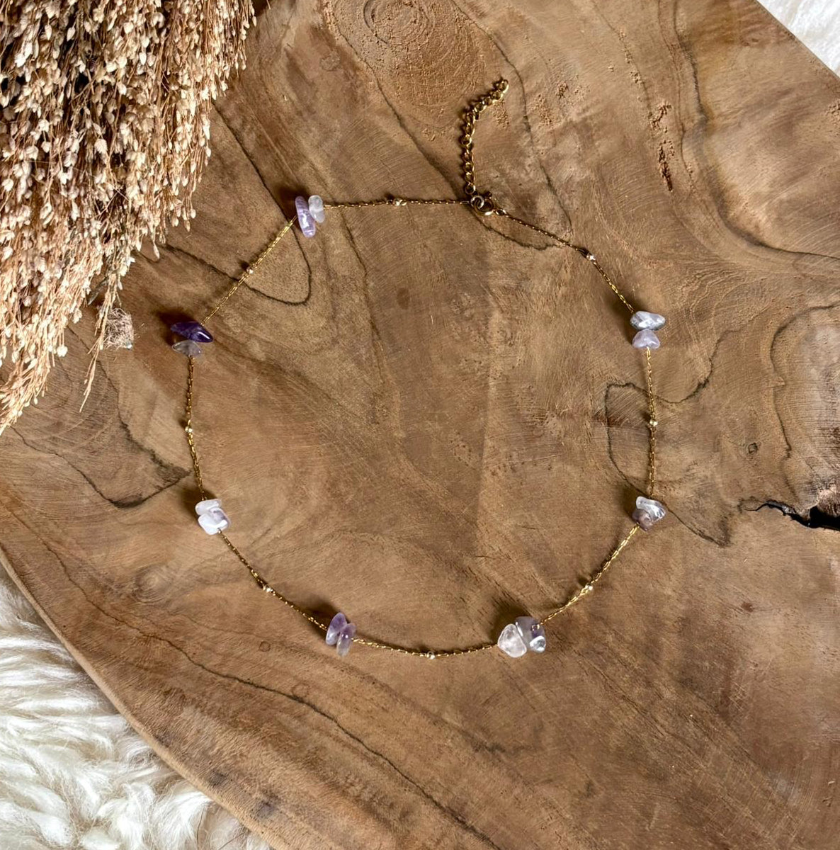 Goudkleurige ketting Lumi met paarse amethist op een houten schaal