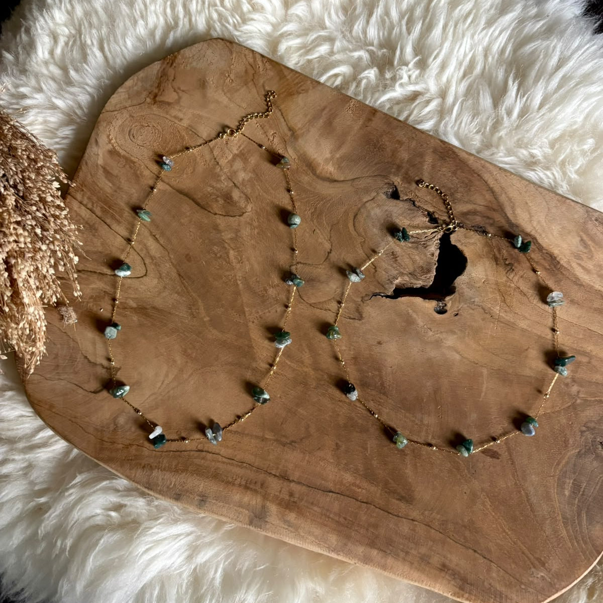 Twee goudkleurige kettingen Lumi met groene mosagaat op een houten plank